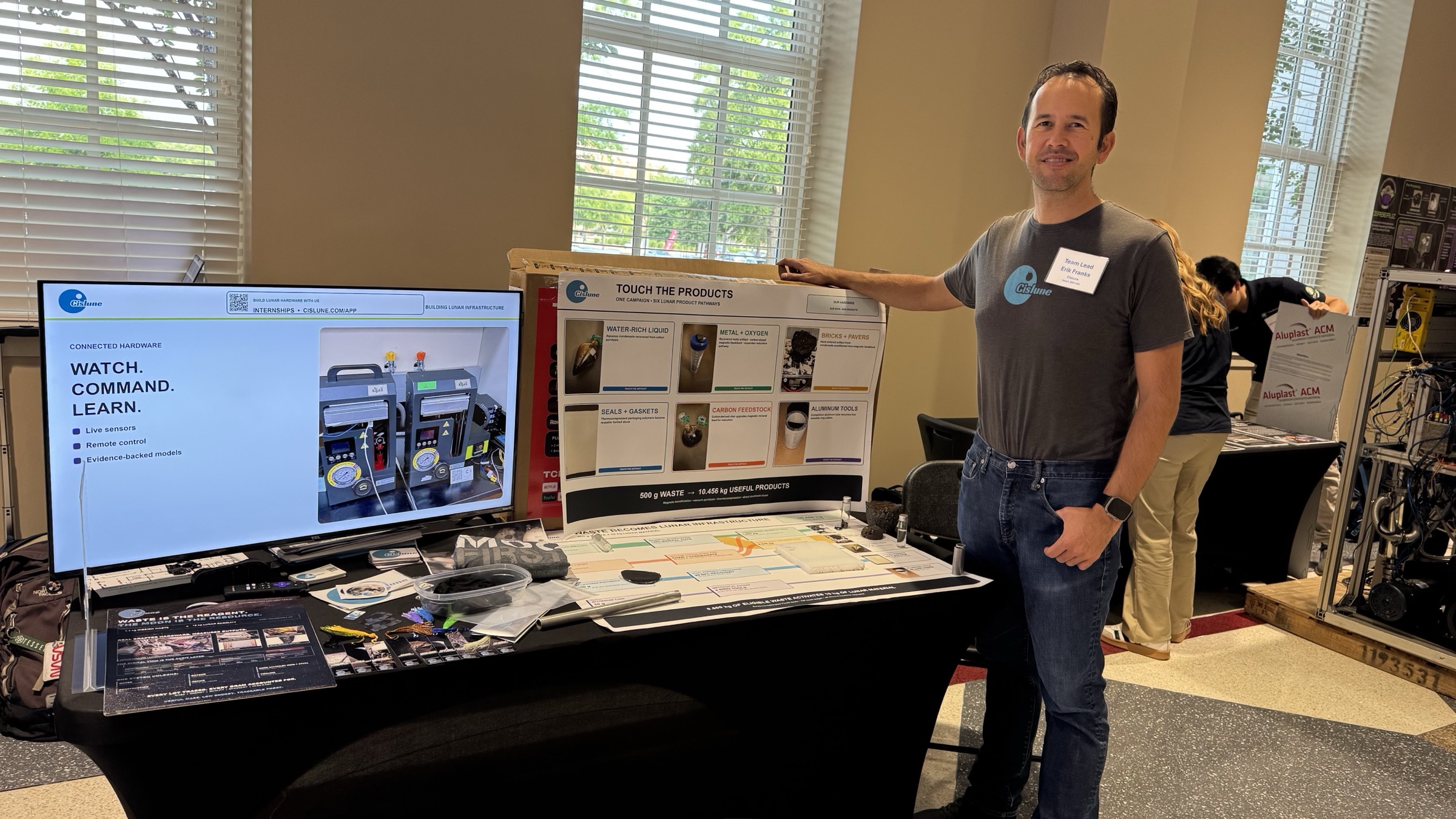 Erik Franks stands beside Cislune's CRAFTER exhibit and physical product samples at the NASA LunaRecycle Challenge finals.